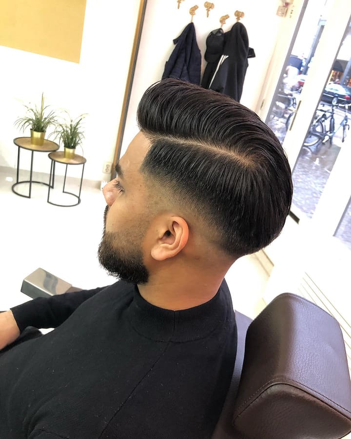 Man met een strakke pompadour, skin fade en verzorgde baard, in profiel in de barberstoel